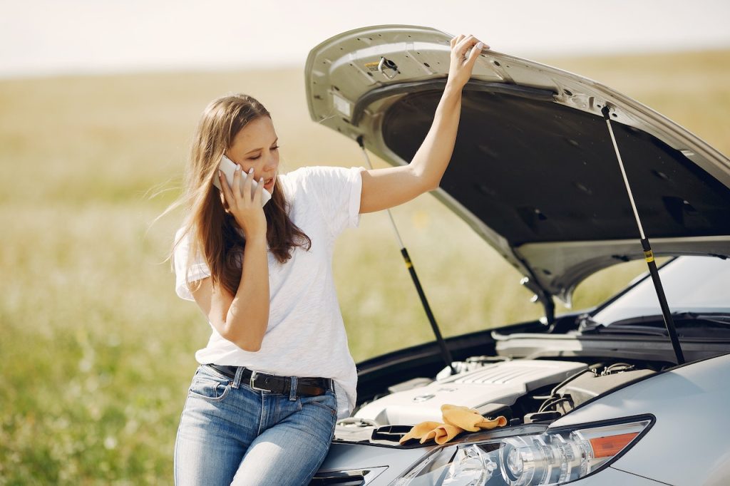 woman sitting on a car bonnet and calling for help