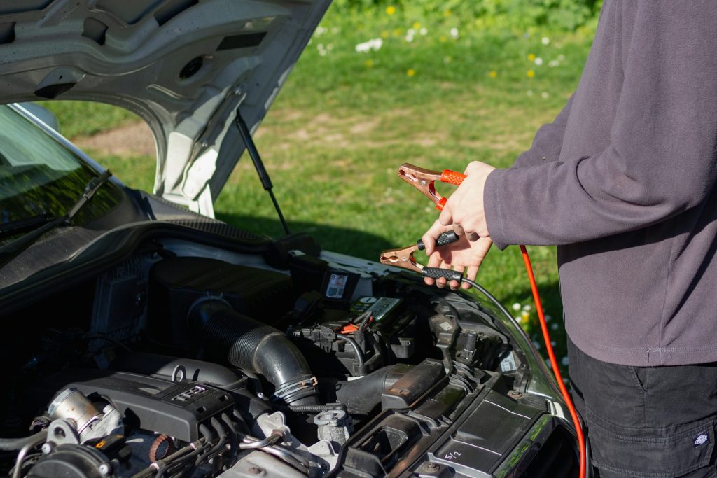 man clipping jump starter cables onto a car battery